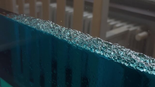 Blue water with floating bubbles in a flat tank create patterns on the surface, illustrating fluid dynamics, buoyancy and surface tension.