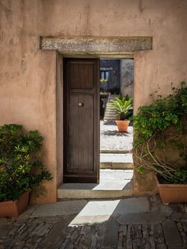 Inviting rustic entrance in a Sicilian village, framing a sun-drenched stone courtyard with potted palms and traditional Mediterranean architecture.