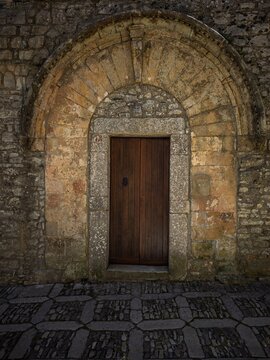 Historic Sicilian doorway in Erice, showcasing intricate ancient masonry, a massive stone arch, dark wood panels, and textured cobblestones in dramatic light.