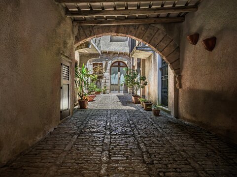 Atmospheric Mediterranean travel photo showcasing a secret covered stone passage opening into a sunny courtyard in Erice, ideal for Sicilian travel guides and cultural media.