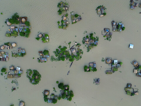 Aerial view of flooded landscape with small islands of houses, trees, and boats in the water in Rajshahi District, Rajshahi Division, Bangladesh.