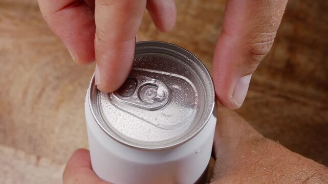 Macro shot of a hand opening a cold aluminum can of carbonated drink covered with water droplets. Perfect for refreshing summer concepts, commercial use, and product promo.
