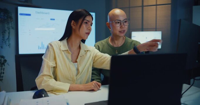 Young Asian businesswomen team meeting work on laptop at office night. Corporate teamwork collaboration, financial report analysis, strategy project planning, colleague development support concept.