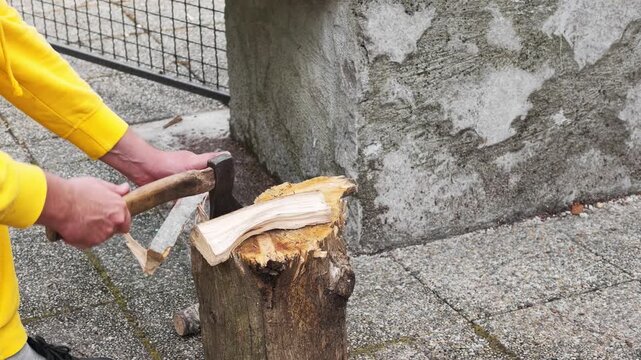 Video showing a person in a yellow sweatshirt splitting a piece of firewood with an axe on a wooden stump