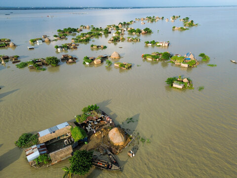 Aerial view of flooded rural landscape with small islands featuring traditional houses, thatched roofs, and wooden boats in the water in Rajshahi District, Rajshahi Division, Bangladesh.