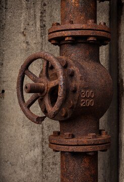 A heavily rusted iron industrial water valve on an old pipe against a textured concrete wall, representing decay and maintenance