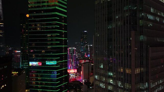 a stunning wide-angle shot of an urban skyline at night, featuring tall buildings with illuminated windows and vibrant red and green lights. the dramatic cityscape showcases glass and metal.