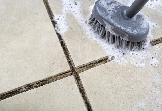 A scrubbing brush cleaning dirty floor tiles with soapy water and foam for home maintenance