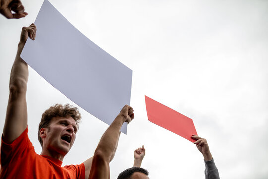 People holding blank protest signs against a cloudy sky.