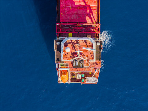 Aerial view of a large cargo ship deck with red surfaces, radar equipment, and a lifeboat, sailing on deep blue sea in Lemesos, Lemesos, Cyprus.
