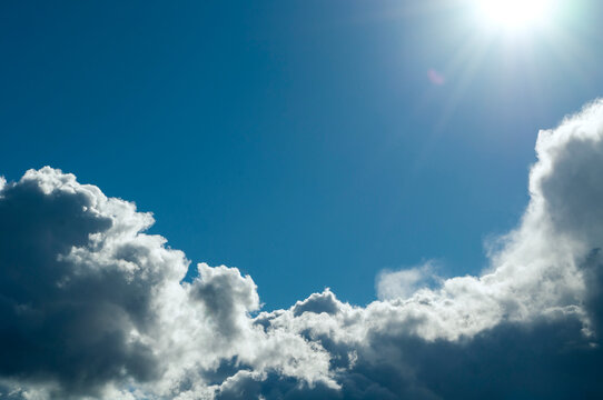Sky background. Bright sun flare shining, fluffy white clouds and a clear blue sky in an open sunny, daytime atmosphere