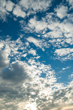 Blue dramatic sunset sky landscape background filled with small white clouds. Thin power lines crossing the lower part of the open airy scene