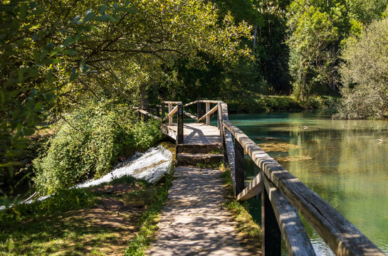 Pasarela de madera bordeando las aguas tranquilas y cristalinas del manantial del r&iacute;o Ebro en Fontibre, rodeada de bosque