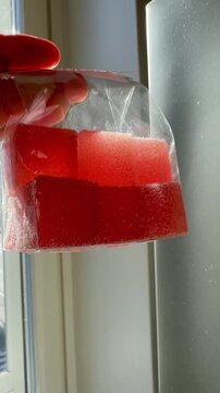 Hand Holding Red Jelly Candy Cubes Against Sunlight Vertical