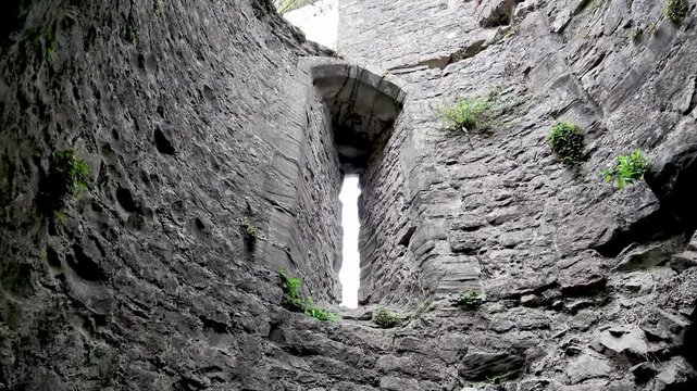Weathered stone walls rise around a narrow arrow slit window as the camera looks up through the ruined castle interior. panning shot