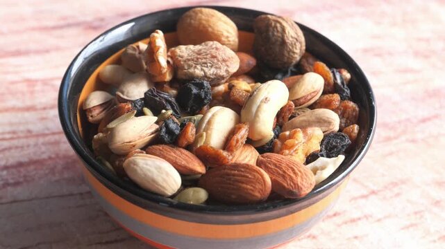 Bowl full of mixed nuts and dried fruits moving slowly on a textured surface, healthy snack footage