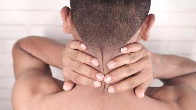Man experiencing neck pain and discomfort, self-massaging his nape and shoulders in a static shot, offering a back view of his upper body