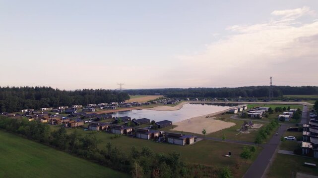 Aerial ascend showing recreational Hoge Hexel bungalow park with summer homes surrounding a lake with beach patch