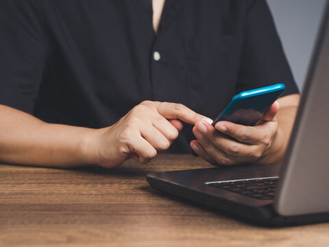 Person using smartphone beside laptop on wooden desk