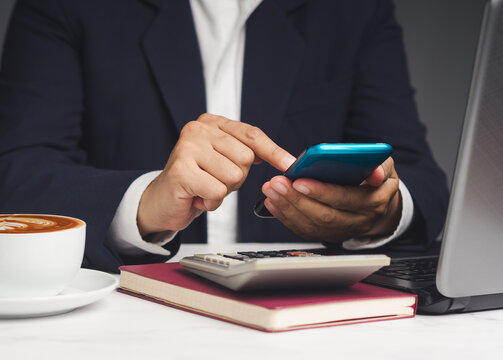 Person using smartphone with calculator and laptop on desk
