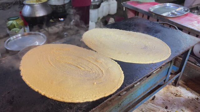 Fresh dosa batter spread across a hot iron griddle releases steam while cooking at a traditional Indian street food stall