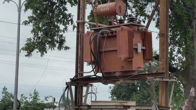 Static footage of a pole mounted electrical distribution transformer with cables insulators and power lines in an outdoor urban setting