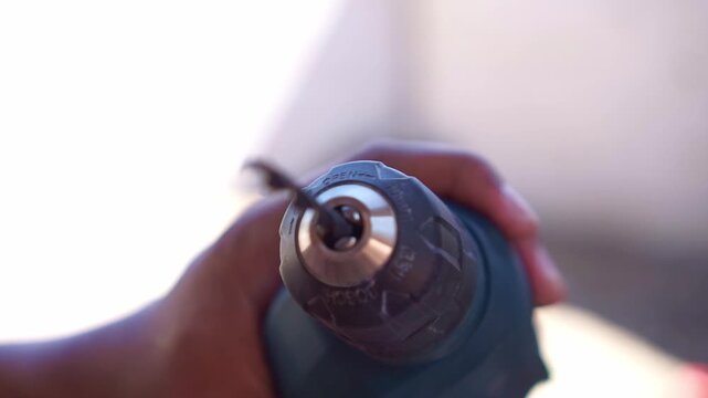 Person attaching drill bit to electric drill chuck, close up shot, hardware tool preparation, workshop footage scene.