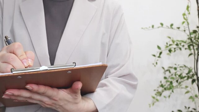 クリップボードの書類に記入する人の手元