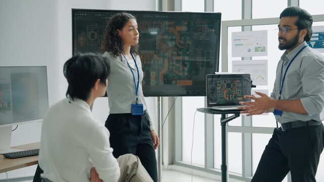 Engineering professionals collaborating on circuit board design while discussing electronics, digital technology, and product development in a modern technical workplace.
