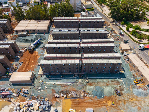 Aerial view of modular construction site with rows of brown container-style buildings, heavy machinery, and earthworks, Lemesos, Lemesos, Cyprus.