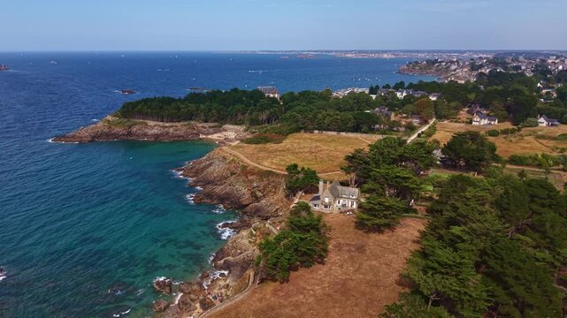 Panorama drone shot of rocky Horn of the Ghoul headland or Cor de la Goule aux Fees beachside and The tip of Roche Pelee with turquoise water and nearby homes, Dinard, Ille-et-Vilaine, France