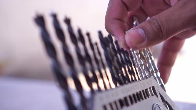 Hand selecting drill bit from tool case, close up shot, metal drill bits set, workshop hardware organization footage.