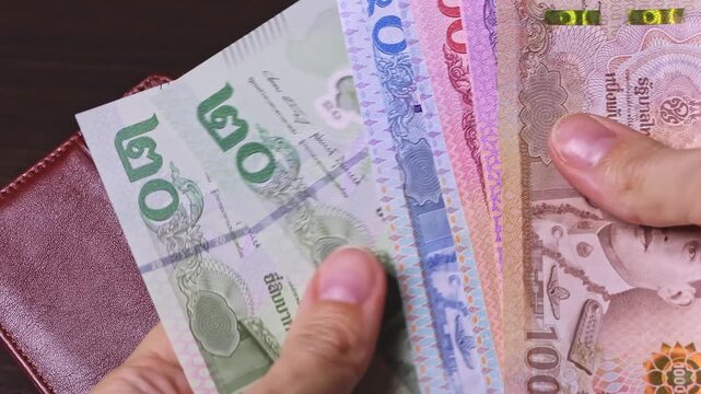 Female hands count Thailand baht notes (THB) and put them in a brown leather wallet. Thailand cash money, wealth and success, financial profit and security concept. Close-up view