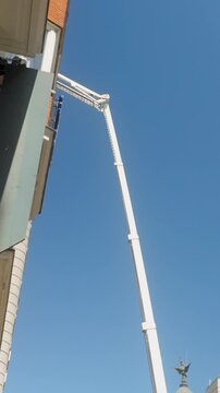 A long white telescopic crane arm extends high above the streets of Madrid, Spain, positioned near historic architecture and a clear blue sky.