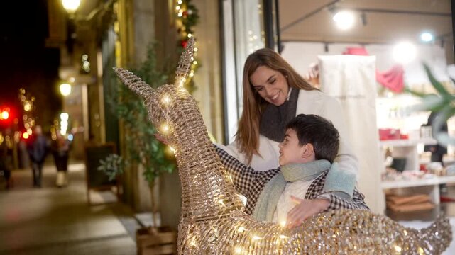 Happy mother and her little boy enjoying the festive season together, looking at a charming light up llama decoration while strolling through the beautifully illuminated city streets at night