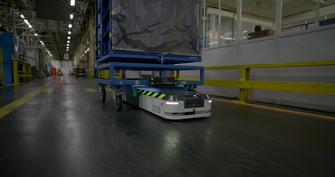 Autonomous mobile robot transporting a heavy blue cargo rack through a large industrial warehouse facility	