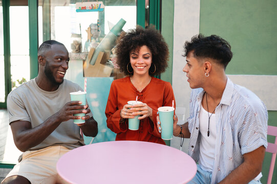 Diverse young friends enjoying contemporary cafe culture, laughing, toasting outside on a summer day