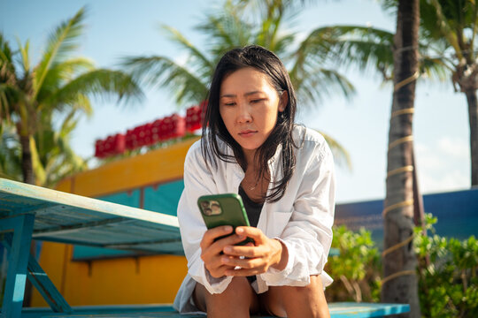 Cheerful woman talking on a smartphone during a sunny day at a tropical beach on summer vacation