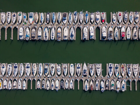 Aerial view of Sausalito Houseboats docked in neat rows at the marina, showcasing white sailboats and motorboats moored along wooden piers in Sausalito, California, United States.