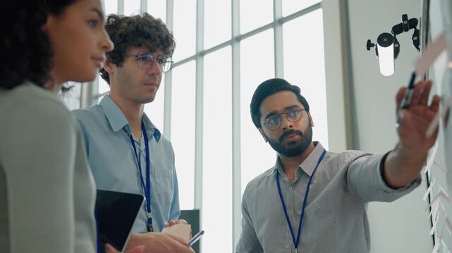 A group of engineers collaborating around a whiteboard while discussing technical ideas, project plans, and technology development in a modern workplace.
