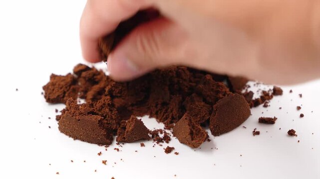 Dried coffee puck isolated on white background, soft focus close up. A hand drops some coffee grounds slowly. White background profile shot of the hand releasing the grounds. 