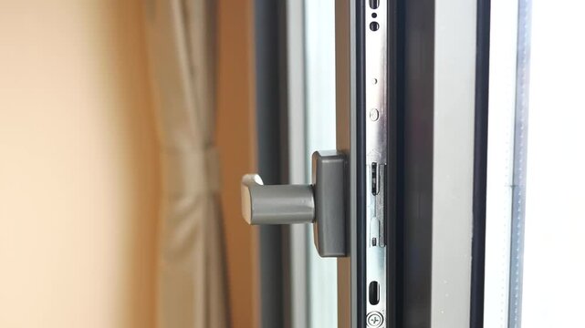 Close-up of a hand turning a window handle to open and close a modern white plastic window frame, showing the locking mechanism in motion