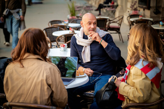 Three friends sitting at street cafe and talking while having coffee