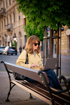 Confident mature woman with laptop sitting on the street in a European city