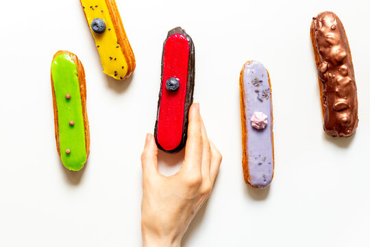 Hand serving colorful eclairs on plate - cozy dessert sharing moment with elegant French pastries, top view