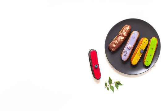 Colorful gourmet eclairs with glazed topping on plate - modern pastry flat lay in soft natural light, top view dessert concept