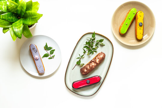 Assorted French eclairs with chocolate, berry and mint icing on plates. Elegant sweet food background, top view