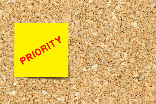 Yellow note paper with word priority on cork board background with copy space