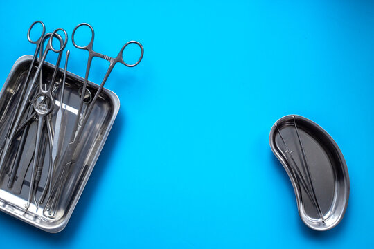 Sterile surgical instruments and tools - scalpels, scissors and others - in a stainless tray on blue background, top view