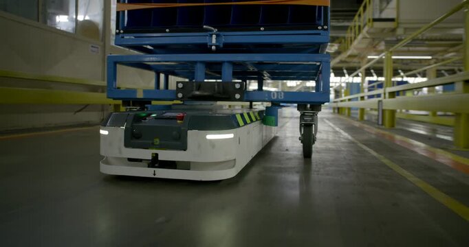Autonomous mobile robot transporting a heavy blue cargo rack through a large industrial warehouse facility	